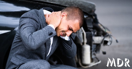 man holding his neck in front of a car accident
